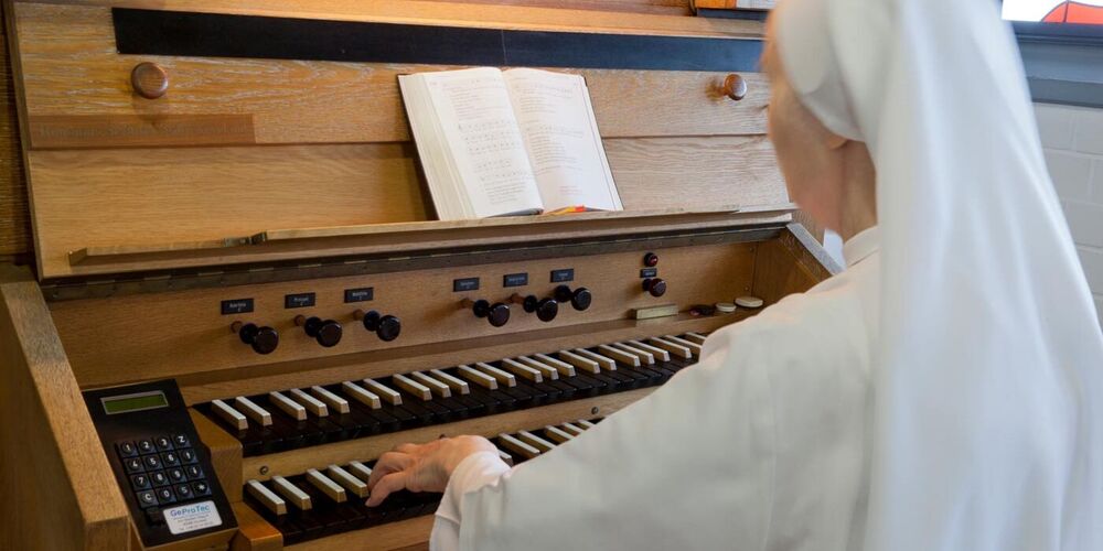 Eine Nonne sitzt an einer Orgel und spielt etwas auf dieser. 